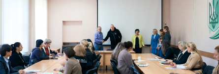 В світлому залі за столом сидять учасниці зустрічі. Перед ними біля стіни заступник голови Рівненської ОДА Олександр Терещенко тисне руку одному із лекторів. Біля нього праворуч стоять інші представниці, які проводитимуть навчання