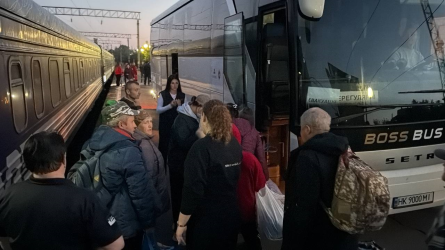 На фото — прибуття евакуаційного потяга. Люди виходять із вагонів та прямують до автобуса, який зустрічає евакуйованих і допомагає їм дістатися до місця тимчасового проживання.