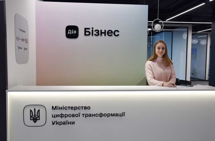У офісному центрі "Дія Бізнес" біля стійки стоїть усміхнена працівниця цього офісу, молода дівчина, у світлій блузі