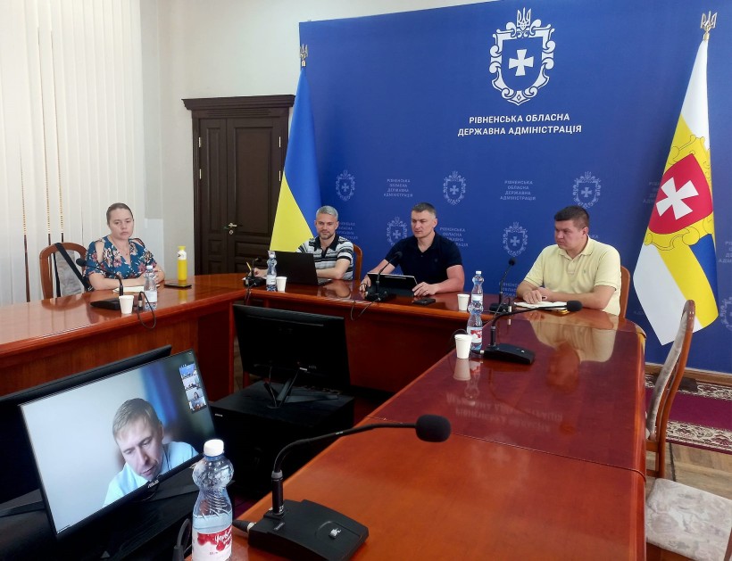 Учасники онлайн-наради сидять за столом на фоні банера з написом "Рівненська обласна державна адімінстрація" та Гербом Рівненської області