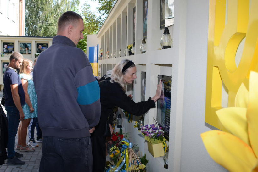 Рідні стоять біля стіни пам'яті, де портрети воїнів загиблих у війні