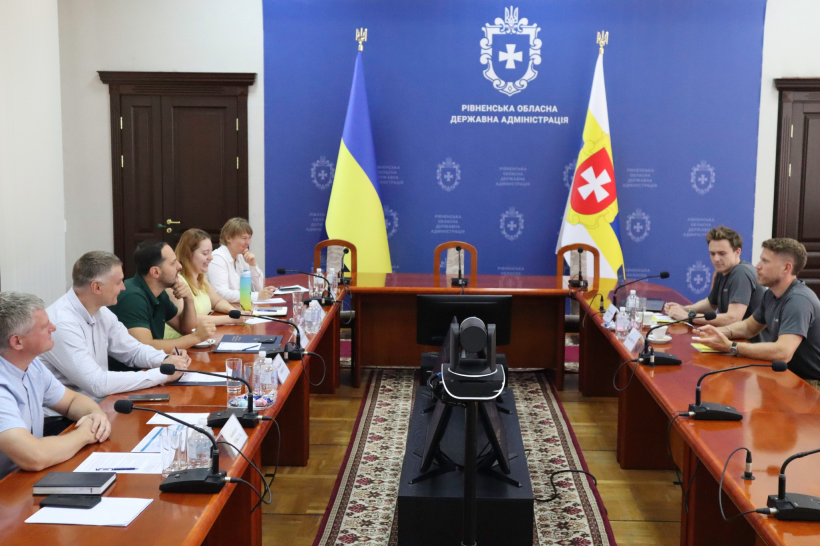 Учасники зустрічі сидять у залі за столом один навпроти одного та спілкуються
