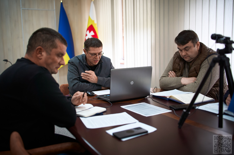 Троє чоловіків сидять за столом, перед ними лежать документи, стоїть ноут-бук та камера для трансляції. В центрі Сергій Подолін, який проводить онлайн-нараду