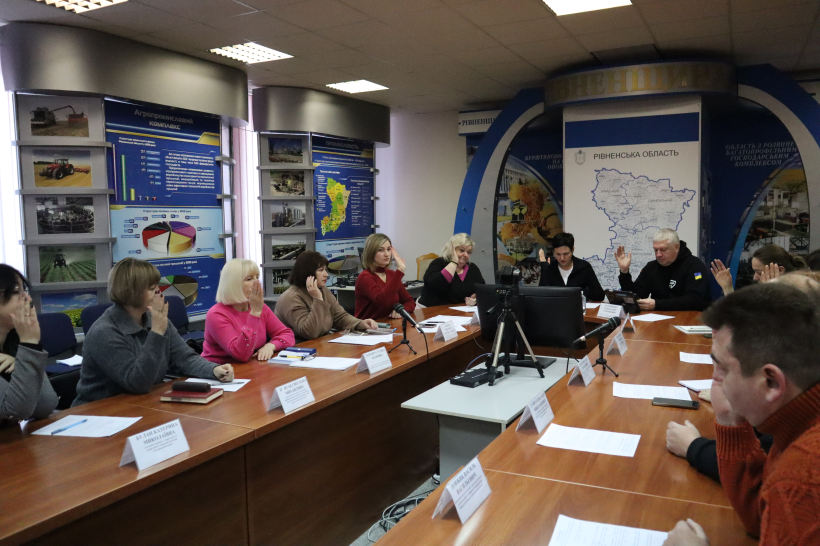 Учасники зустрічі сидять за столом та голосують піднявши руку