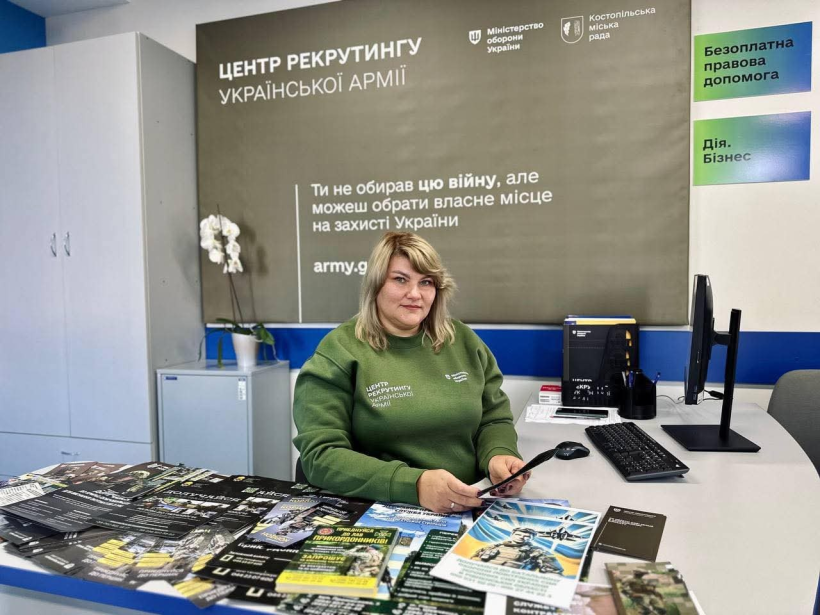В кабінеті за столом сидить працівниця рекрутингового центру. перед нею на столі  лежать буклети