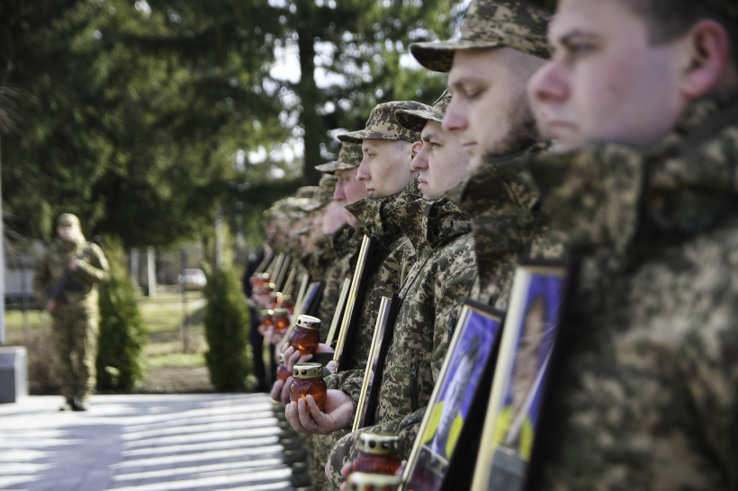 Військовослужбовці тримають у руках портрети загиблих аід ракетного удару нацгвардійців та запалені лампадки