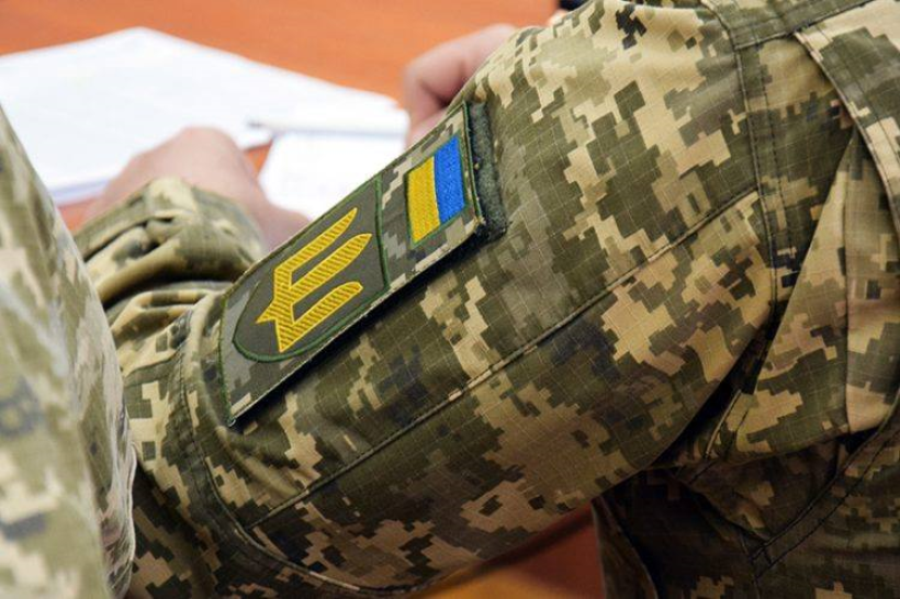 Фото ілюстративне - вид зі спини: сидить військовий у піксельній формі із шевронами ЗСУ та щось пише