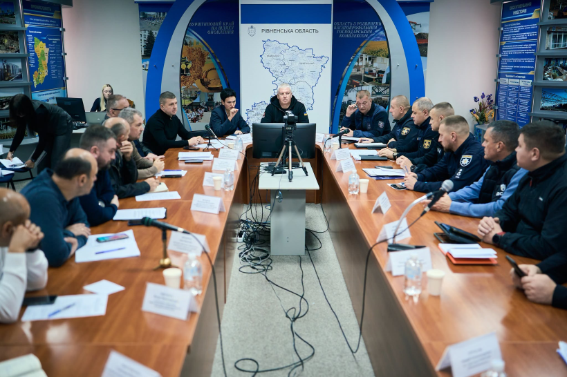 Учасники наради сидять за столами у конференц-залі та обговорюють робочі питання. У центрі столів розміщені монітори й обладнання для відеозв’язку.