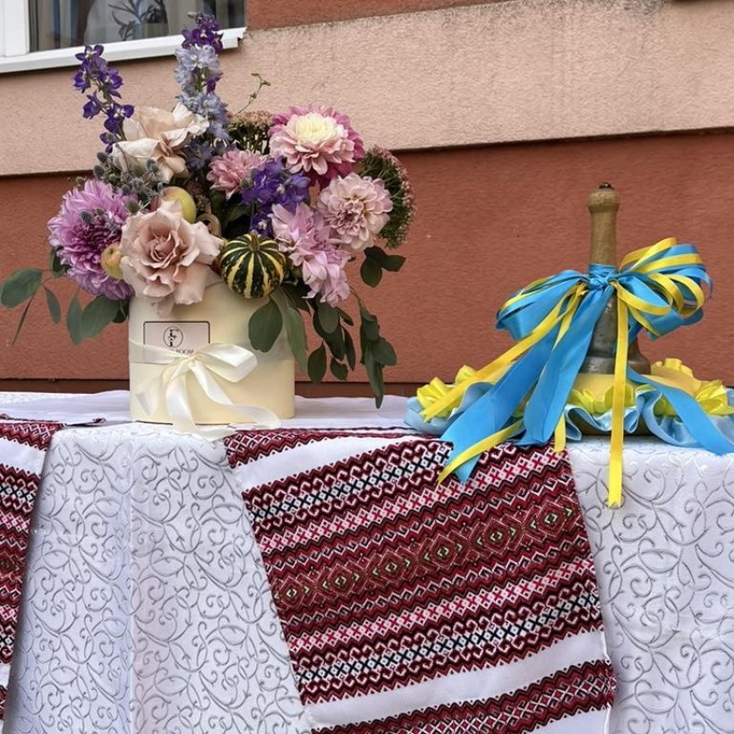 На столі букет квітів, дзвінок з жовтою та блактиною стрічками