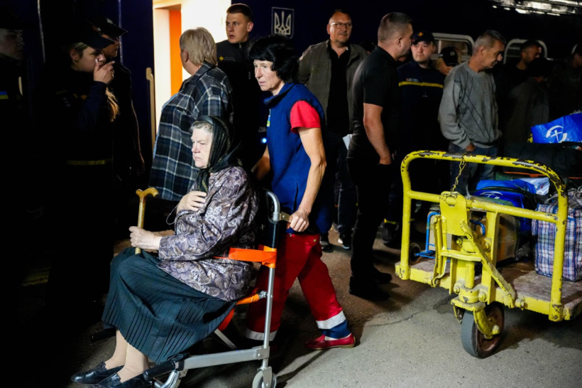 З поїзда зустрічають вимушено переміщених осіб: на кріслі колісному сидить жінка старшого віку, вона в чорній хустині, у руках жінка тримає палицю, на її обличчі туга. Її везе жінка медик, поруч стоять багато чоловіків і жінок. На вулиці темна пора доби, лише у вагоді яскраво світиться світло