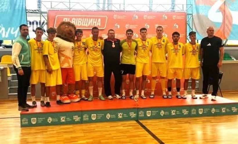 Спортивна чоловіча команда у жовтих костюмах вишикувалися на загальне фото. В центрі їхній тренер. У всіх на грудях медалі. Всі щасливі та посміхаються
