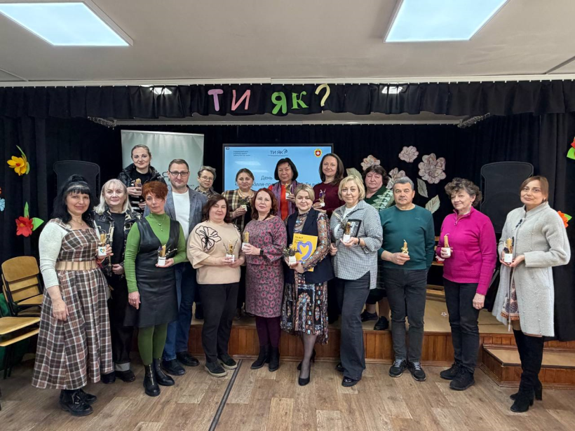 Загальне фото учасників заходу «Позашкілля — простір турботи Ти як?». 16 чоловіків та жінок стоять та посміхаються, тримаючи у руках композиції із сухоцвітів, паперу та свічок