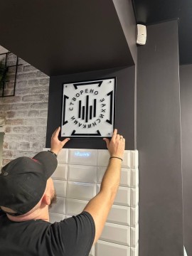 Чоловік кріпить на стіну табличку з логотипом, що ідентифікує бренд “Створено Захисниками”