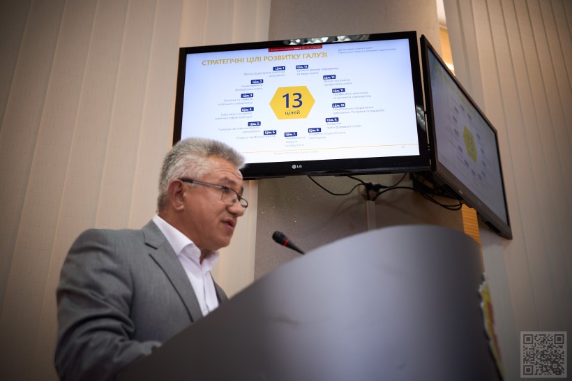 Чоловік за трибуною говорить у мікрофон, позаду нього монітор на якому зазначені 13  стратегічних цілей розвитку освіти Рівненщини