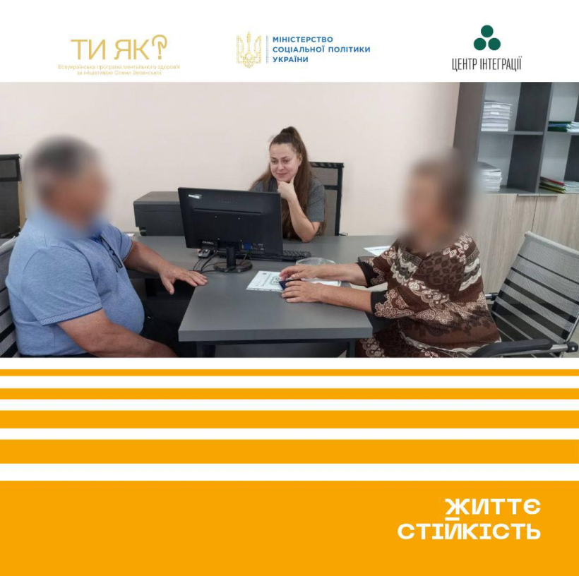 За столом сидять - працівниці Центру життєстійкості та двоє внутрішньо переміщених осіб: чоловік та жінка. Їхні обличчя заретушовані.Працівниці дивиться у монітор комп'ютера і щось записує