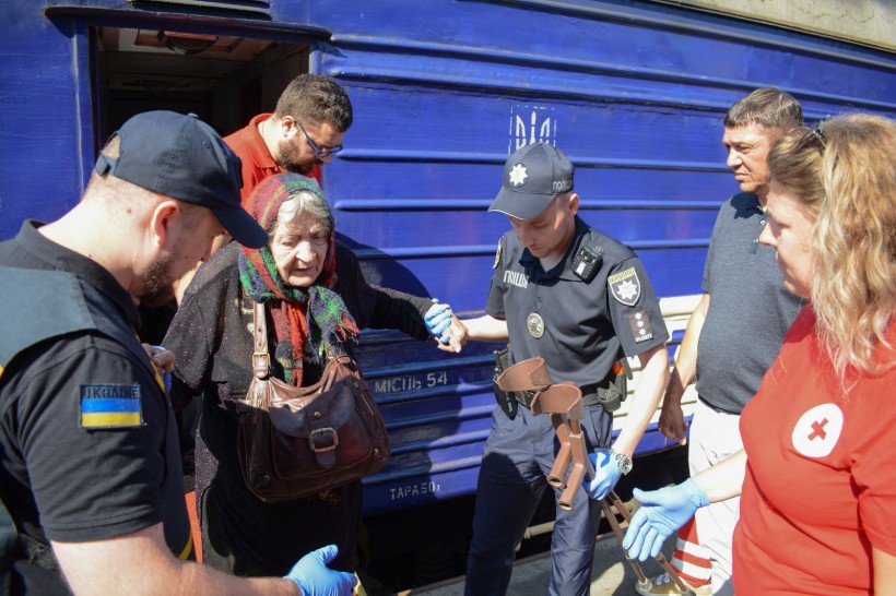 З вагона евакуаційного потягу виходить старенька жінка, яку за руку підтримують поліцейські, працівники ДСНС, Червоного хреста. Серед зустрічаючих і перший заступник голови Рівненської ОДА Сергій Подолін