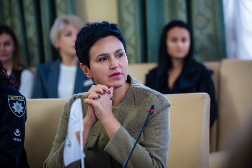 Людмила Шатковська стоїть за столом під час зустрічі та уважно слухає