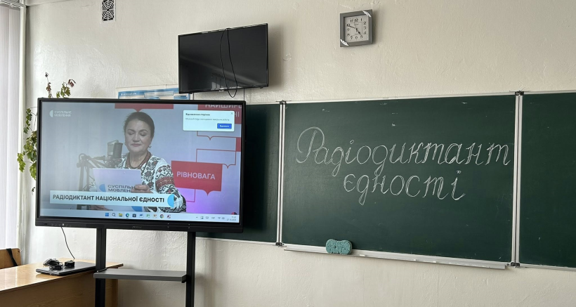 В аудиторії біля дошки всановлено екран з якого Наталія Сумська читає диктант. На дошці крейдою написано: радіодиктант єдності