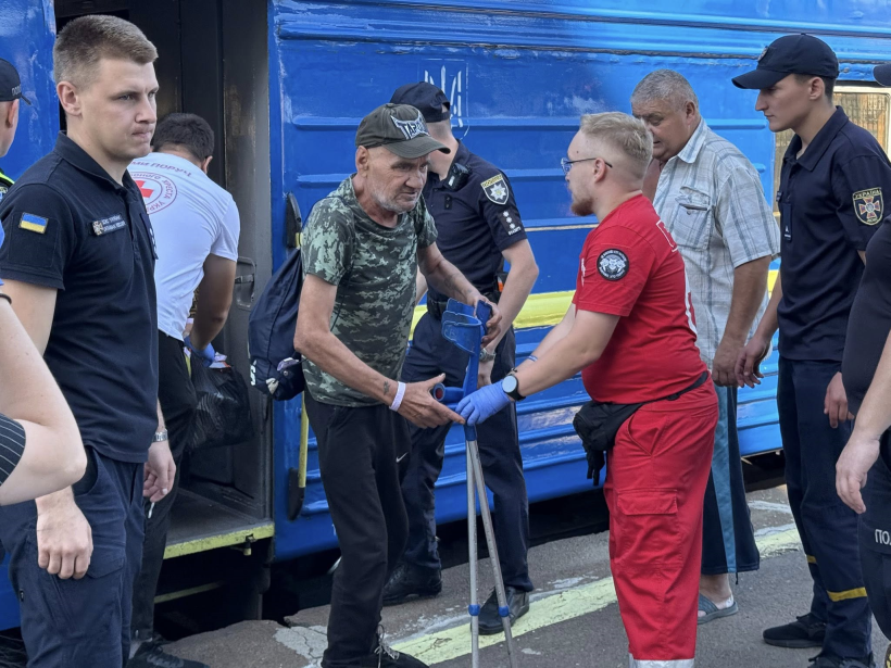 На пероні Рівненського вокзалу представники ДСНС, поліції та Червоного хреста зустрічають переселених громадян. З вагона виходить старший чоловік із сумкою на плечі, йому подають руку щоб допомогти вийти