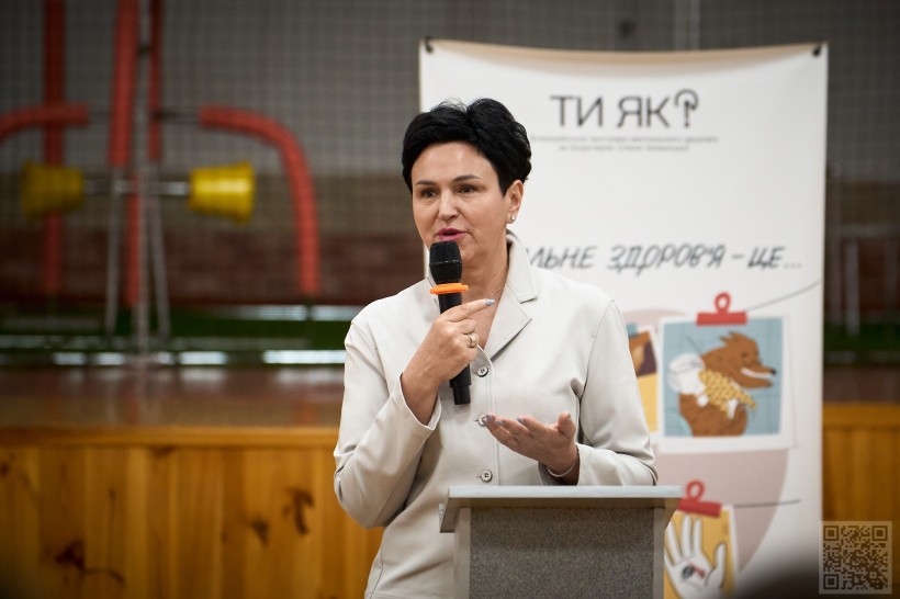 Людмила Шатковська стоїть біля трибуни та говорить у мікрофон
