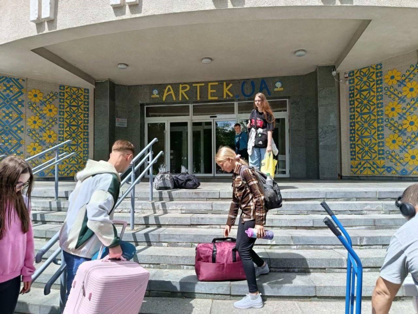 На фото зображено групу дітей, які з валізами заходять у будівлю з написом "АРТЕК.UA".