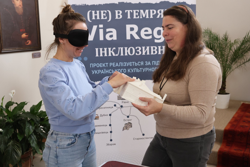 Жінка проводить екскурсію для незрячої іншої жінки яка руками торкається макетів