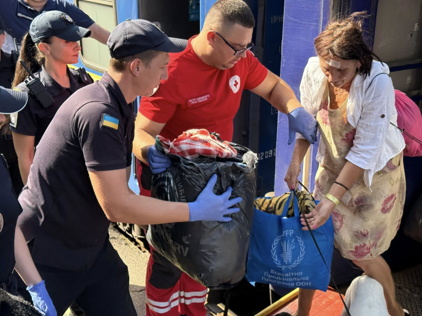 Ппрацівники поліції та Червоного хреста допомагають вийти з вагона старшій жінці та забирають їй з рук сумки