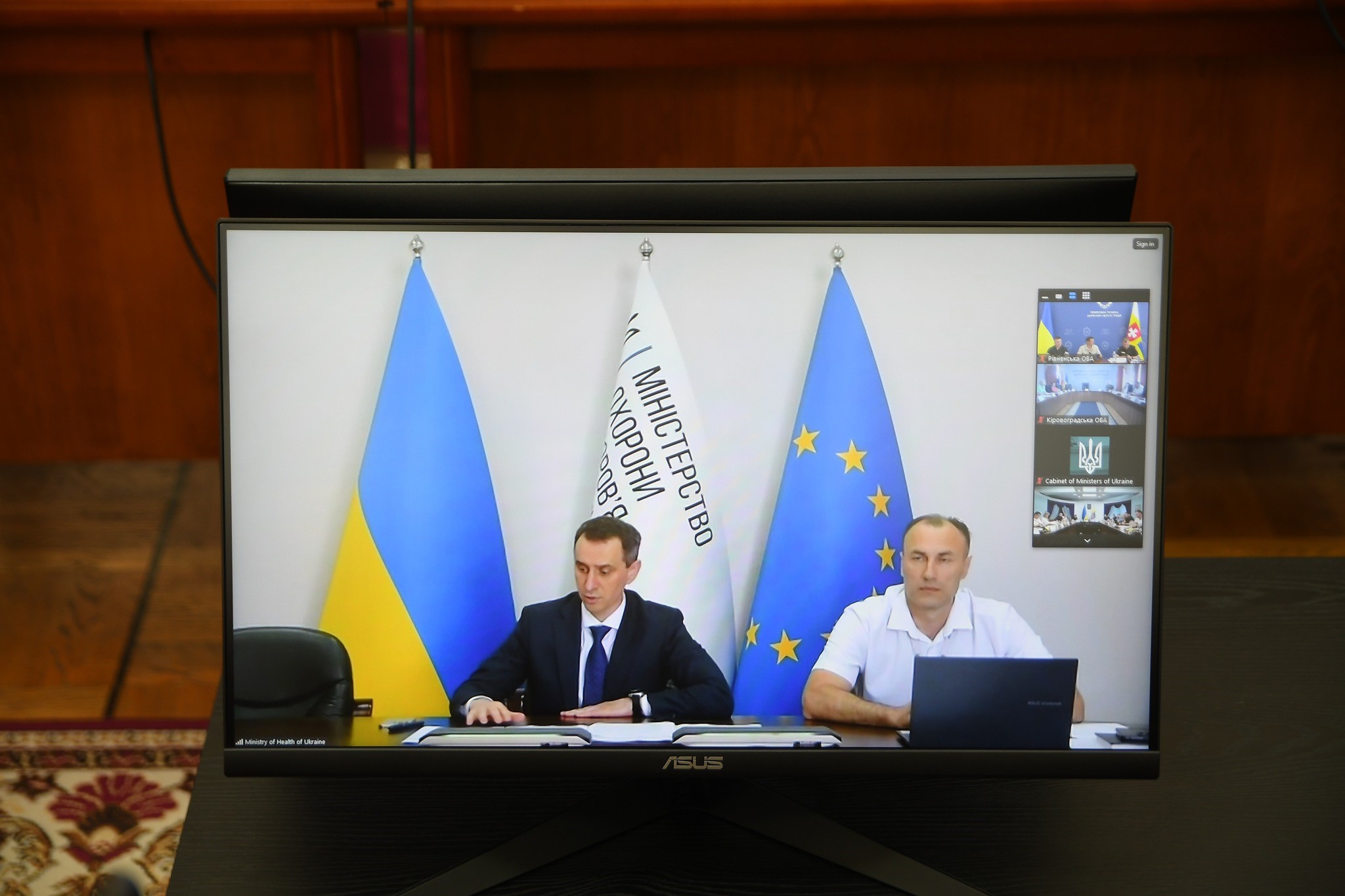 Міністр охорони здоровя України В.Ляшко - за столом під час засідання на фоні Державного прапора України, прапорів МОЗу та ЄС