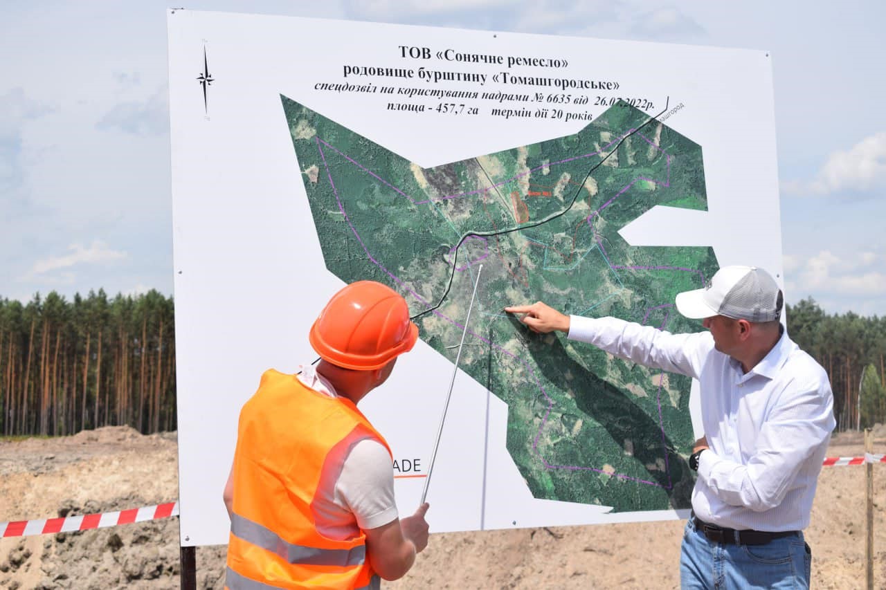 Дві людини біля інформаційного стенду "ТОВ "Сонячне ремесло" родовище бурштину "Томашгородське" з картою родовища