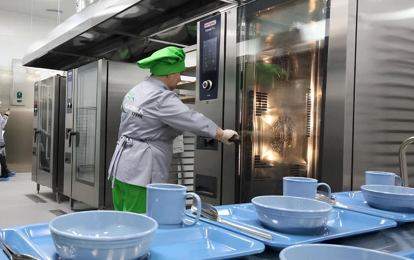 Жінка повар у білому готує на шкільній кухні